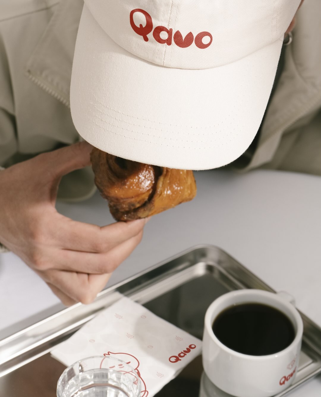 Customer enjoying a pastry while wearing a Qavo-branded cap and using Qavo napkins and mug